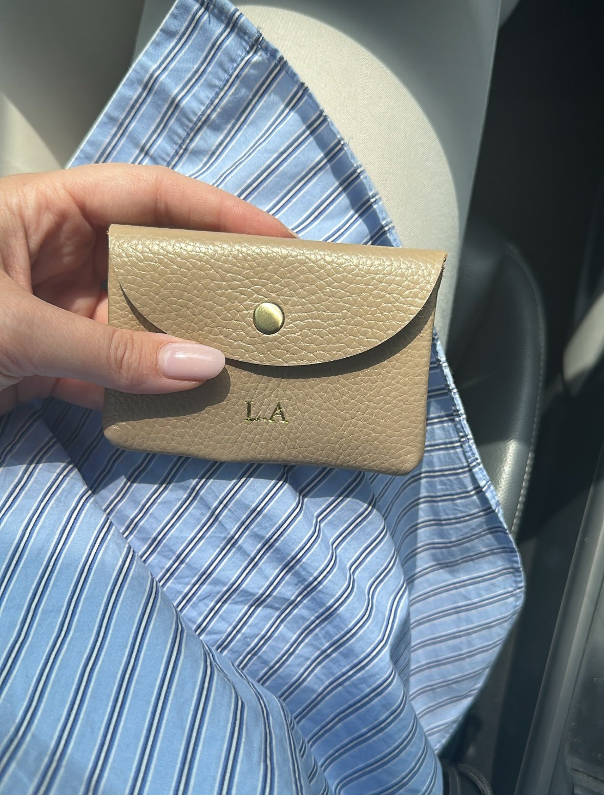 Lala Collection beige leather card holder with gold embossed initials held in hand over a blue striped shirt